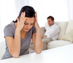 Woman thinking at a table while her boyfriend relaxing on the so