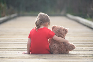 Girl in red dress sitting with teddybear on boardwalk